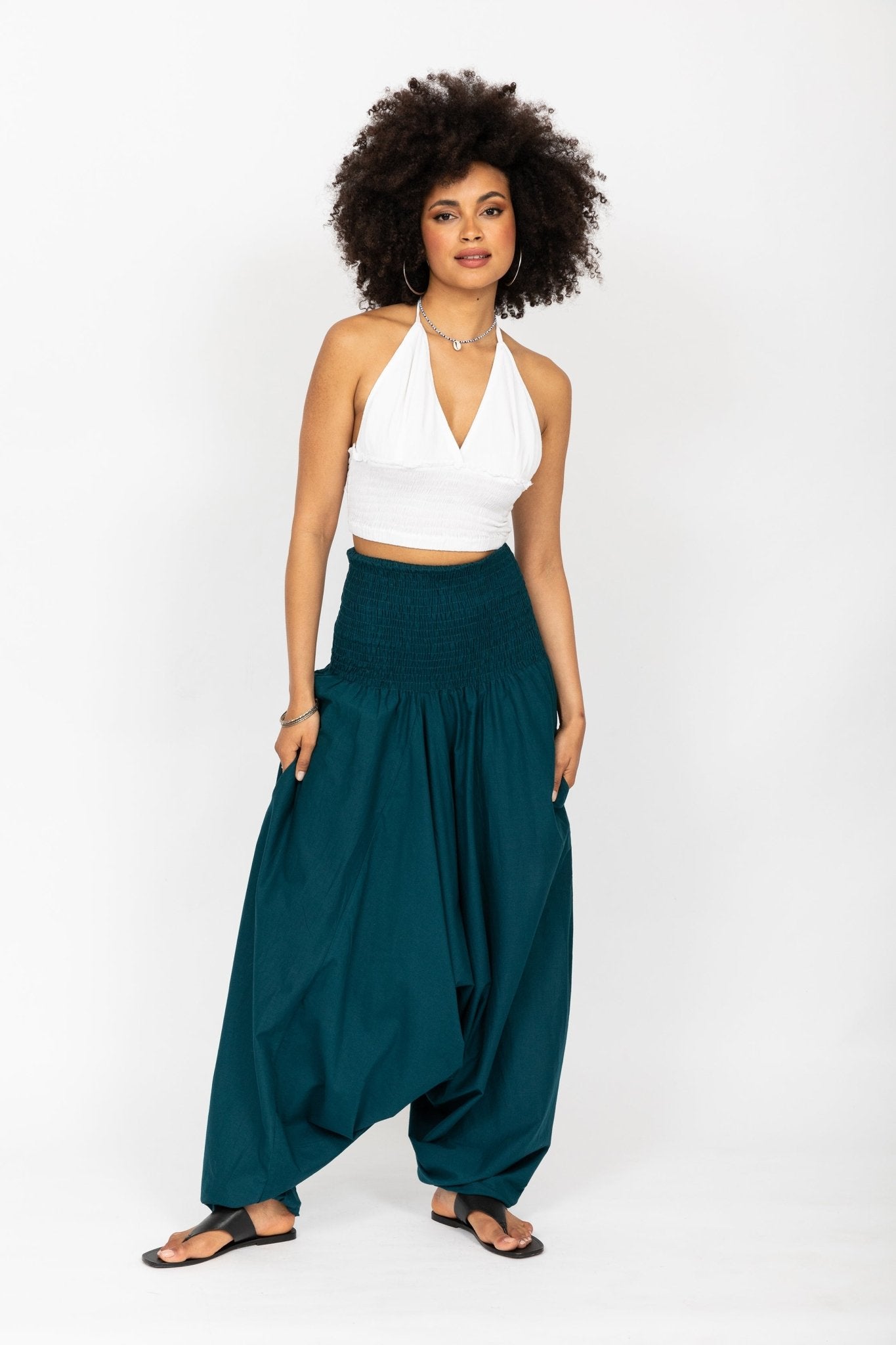 Woman wearing a white top and teal pants on a white background